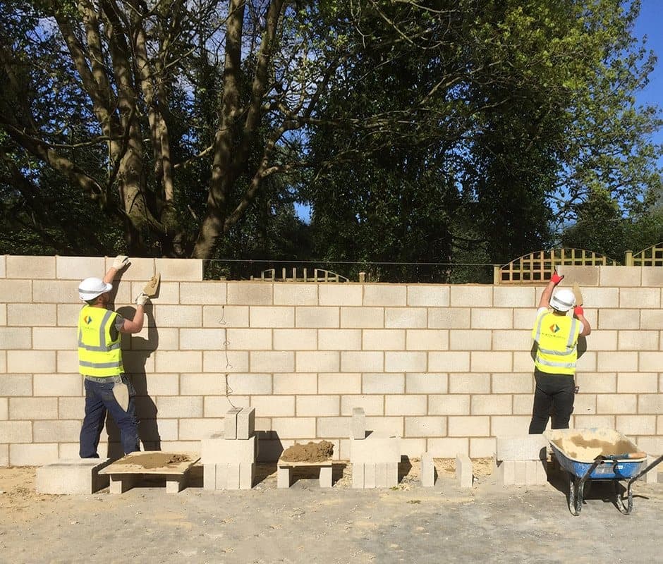 Two bricklayers in hard hats and hi-vis building the blockwork walls