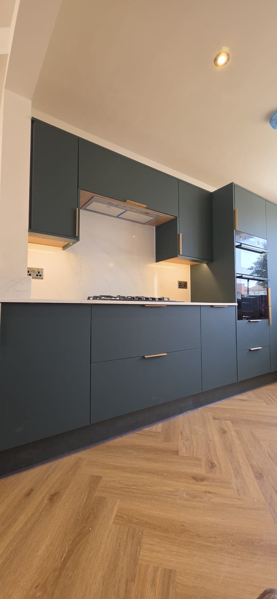 Dark green handleless kitchen with a marble-effect splashback and a gas hob