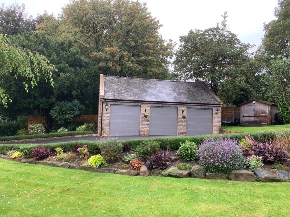 The finished stone garage with three grey doors and a slate roof, seen across the garden