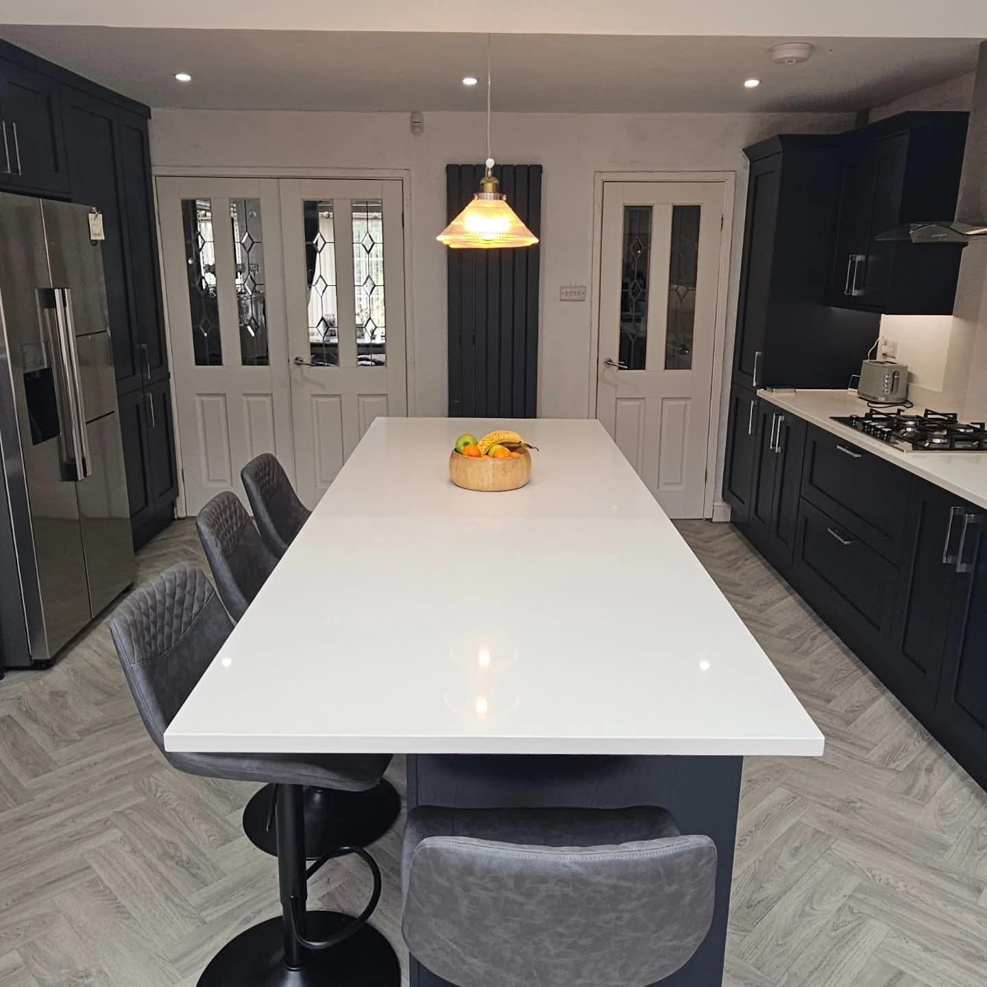 Finished kitchen with a long white-topped island, bar stools and navy shaker units