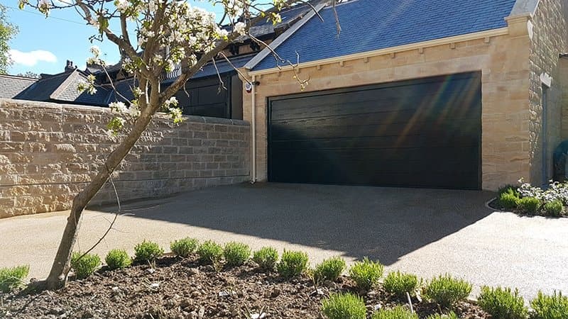 Detached stone garage with a dark sectional door and the driveway